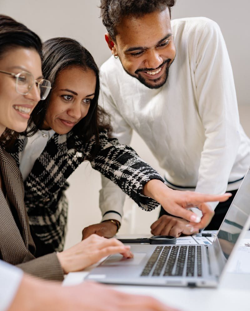 A diverse group of professionals working together focused on a shared laptop.