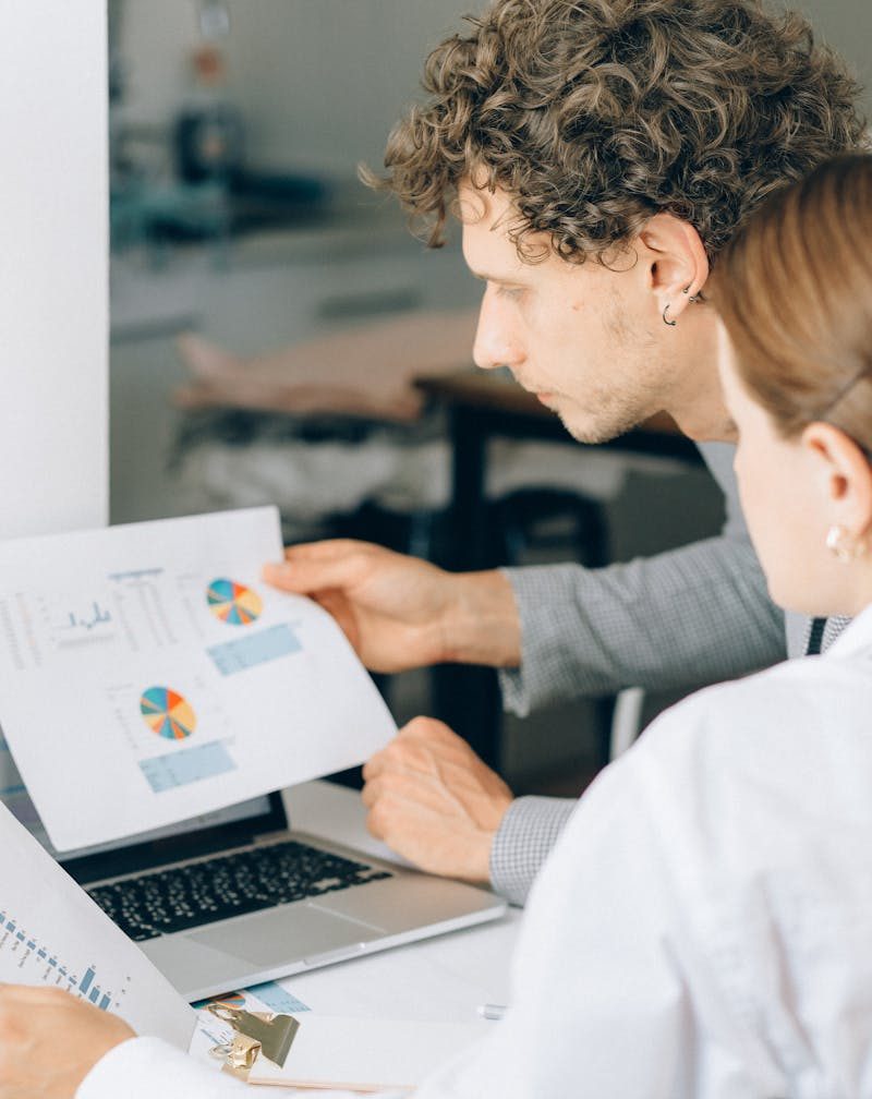 Two business professionals reviewing financial charts and graphs in a modern office setting.